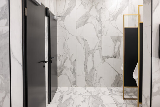 Modern public washroom interior with marble tiles and black doors