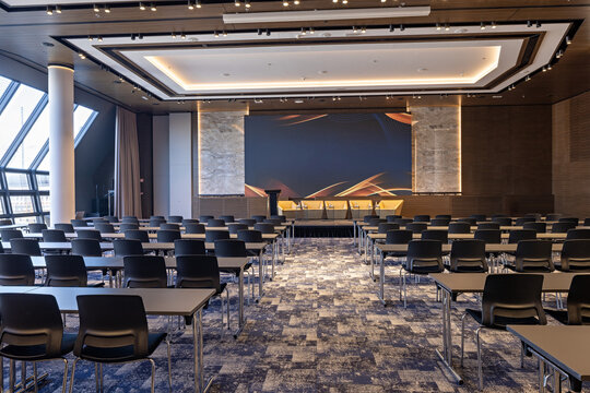 Empty modern conference hall with rows of tables and chairs facing the stage
