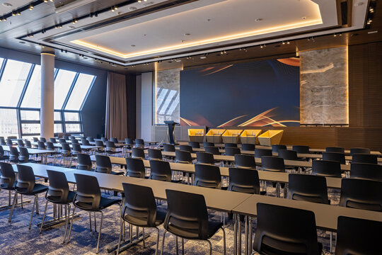 Large modern conference hall with rows of seats desks and big stage screen