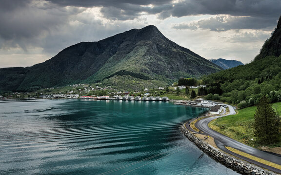 Beautiful Skjolden Fjord Landscape in Norway With Mountain Village, Curving Waterfront Road, Emerald Hills and Moody Cloudy Sky