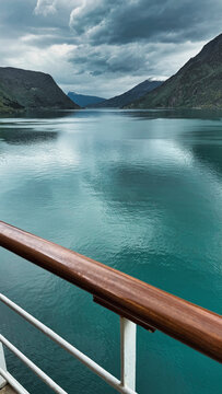 Moody Norwegian Fjord Landscape From a Cruise Ship Railing With Turquoise Water, Storm Clouds and Snow Capped Mountains in Norway