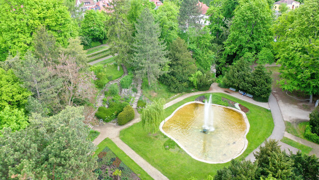Aerial view of the Stadtpark featuring a central fountain in a pond surrounded by walking paths and lush green trees in Forchheim, Bayern, Germany.