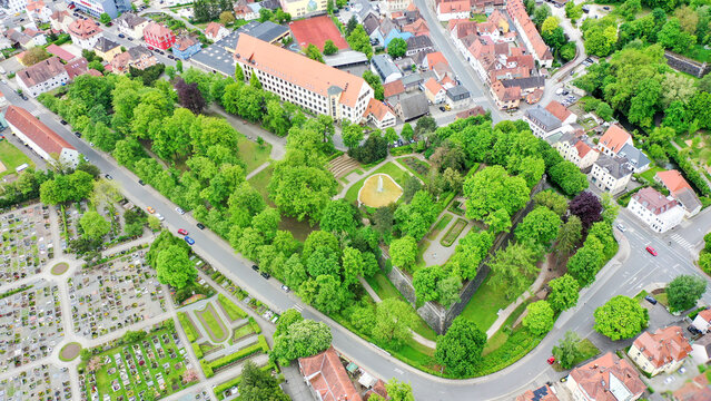 Aerial view of Stadtpark featuring lush green trees, a central fountain, and historic stone walls surrounded by urban buildings and a cemetery Forchheim, Bayern, Germany.