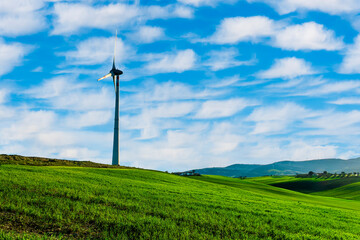 Obraz premium alternative energi power plant with wind turbine in a green summer field with hills and blue cloudy sky on background