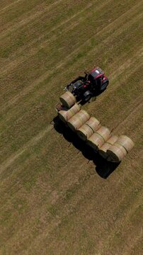A tractor pulls a trailer laden with freshly baled hay across a vast, harvested field, showcasing the bounty of the agricultural season.