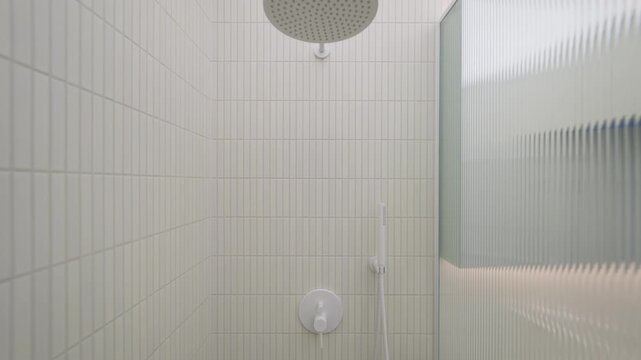 Shower fixture unit features water mixer tap with hand spray and overhead rain head panel inside bathroom stall. Plumbing system equipment provides sanitation utility inside vacant home property.
