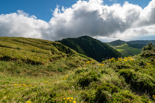 Scenic landscape view of lush green hills, vibrant meadows, and dark forested mountains under dramatic clouds in the Azores