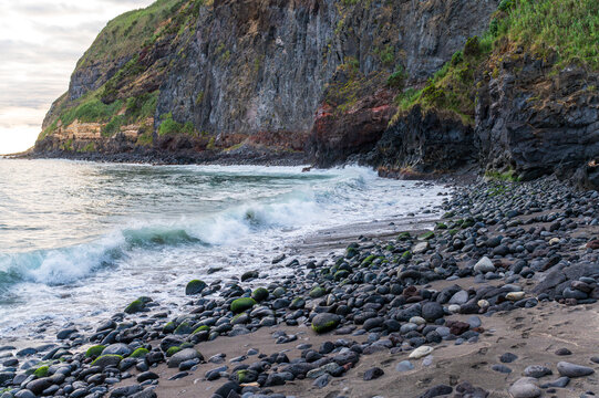 Rugged volcanic coastline with steep cliffs and a dark rocky beach in the Azores