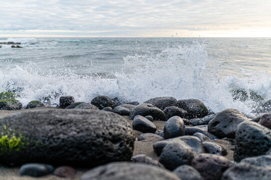 Ocean waves crashing on dark volcanic rocks with green moss on a beach in the Azores