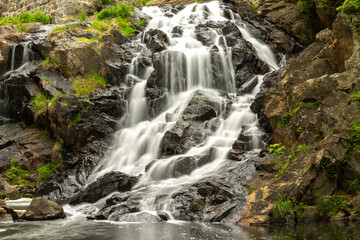 Fototapeta premium Smooth flowing waterfall at Antietam Lake Falls in Reading, PA, captured with long exposure among rocks and lush greenery.