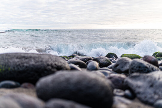 Ocean waves crashing on dark volcanic rocks with green moss on a beach in the Azores