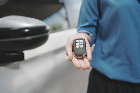 Person holding a car key fob beside a vehicle door and side mirror, suggesting unlocking or remote entry. Shallow depth of field, modern transport and security concept.