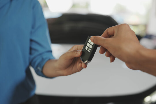Close-up of hands exchanging a car key fob outdoors near a vehicle, symbolizing car purchase, rental.