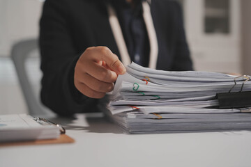 Close-up of office worker handing over thick stack of paperwork with binder clip on desk, blurred...