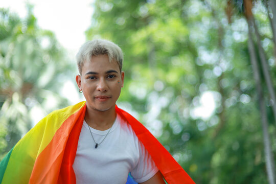 Striking portrait handsome blonde Asian gay man embracing the Pride flag signifying his diverse sexual orientation and LGBTQ identity man who is attracted to other men.