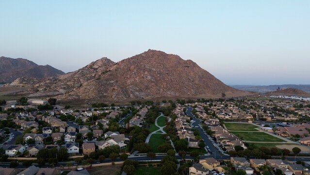 Aerial view of residential neighborhood with green park and rocky mountain at sunset, Perris, California