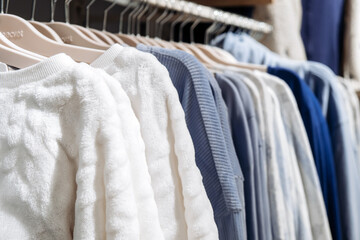 Display of various textured sweaters in neutral and blue tones hanging on wooden hangers in a retail clothing store setting © wedmoments.stock