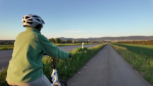 Woman cyclist riding electric bicycle on rural road in evening countryside  