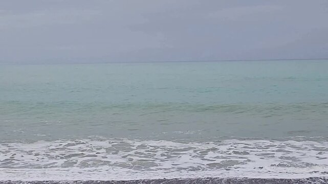 Kaikōura, New Zealand - Shoreline with gentle waves, muted sky and calm New Zealand coast. Gentle waves reach the Kaikōura shoreline under a soft, overcast sky. 