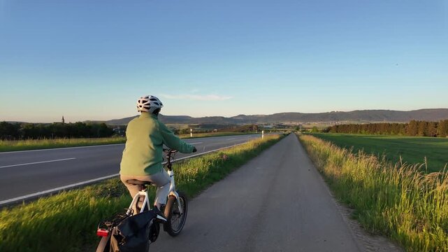 Woman cyclist riding electric bicycle on rural road in evening countryside  