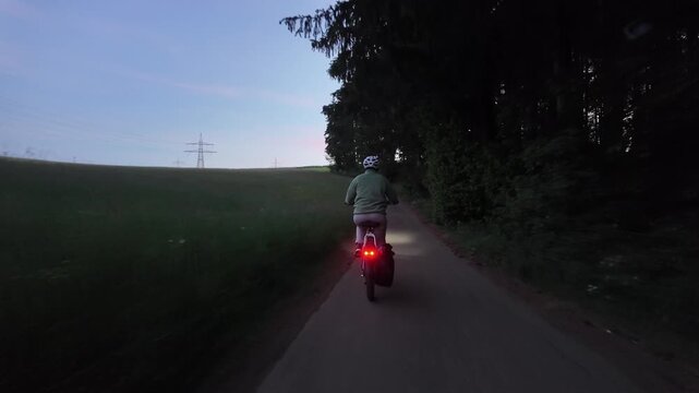 Woman cyclist riding electric bicycle on rural road in evening countryside  