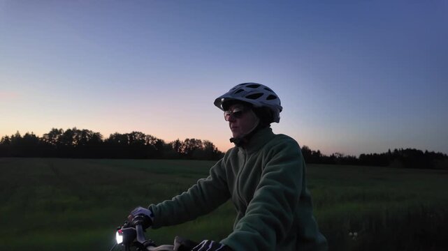 Woman cyclist riding electric bicycle on rural road in evening countryside  