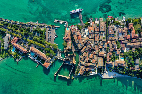Aerial view of Scaligero Castle and the historic town of Sirmione on the shores of Lake Garda with turquoise waters, boats and a parking lot Italy.