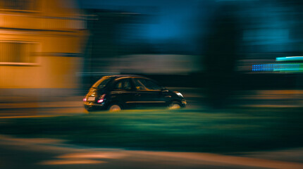 Obraz premium Dark small car travels quickly on an urban street at night Buildings blurred by fast movement