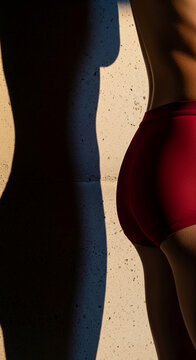 Side profile of a human body in red shorts, with dramatic shadow cast on a textured wall, symbolizing form, light and contrast