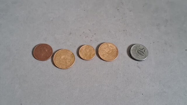Human hand placing various metal coins in a horizontal row on a smooth grey surface