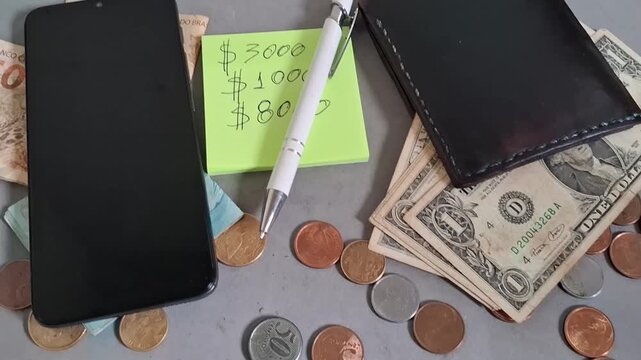 Smartphone and wallet with cash and coins arranged for financial planning on a flat surface