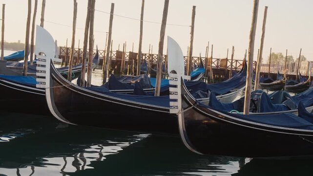 Venetian gondolas with ferro ornament moored, floating on calm morning water
