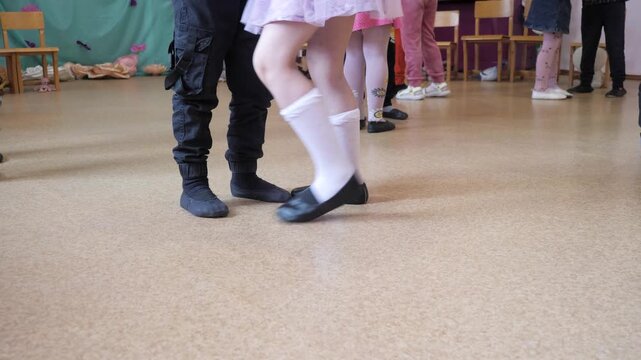 Low angle view of little children feet in soft dance shoes practicing slow waltz performance steps on linoleum floor during kindergarten holiday celebration.