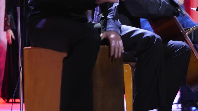 talented musician sitting and rhythmically hitting cajon acoustic wooden box drum instrument with hands on stage during live concert
