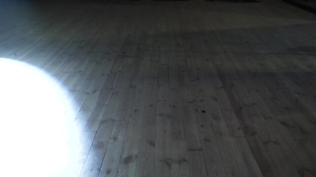 Bright circular white spotlight beams move rhythmically across dark empty wooden floorboards on professional theater stage