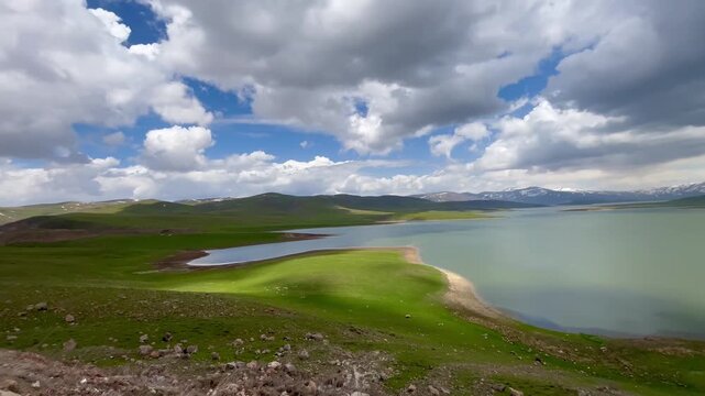 clouds over the lake Scenic wide-angle video of a massive water dam reservoir surrounded by lush green hills under a partly cloudy sky in springtime
