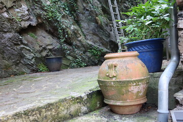 Obraz premium An old decorative clay pot stands near a stone wall in a quiet corner of Cochem, Germany. Green plants and rustic textures create a peaceful atmosphere.