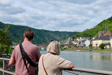 Fototapeta premium Tourists enjoying the scenic Moselle River view in Cochem, Germany. Green hills and riverside houses create a peaceful atmosphere.