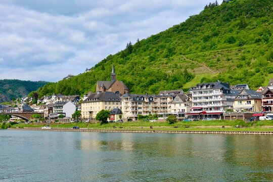 Picturesque riverside town in Cochem, Germany with vineyards and green hills. Calm river water reflects the summer landscape.