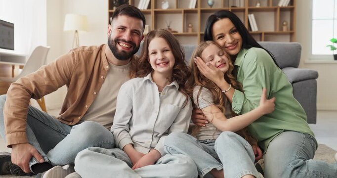 Family parents mother father smiling together, daughters. Children at home with parents, laughing on the floor. Warm lifestyle portrait shows love and happiness. Clear message of family unity.