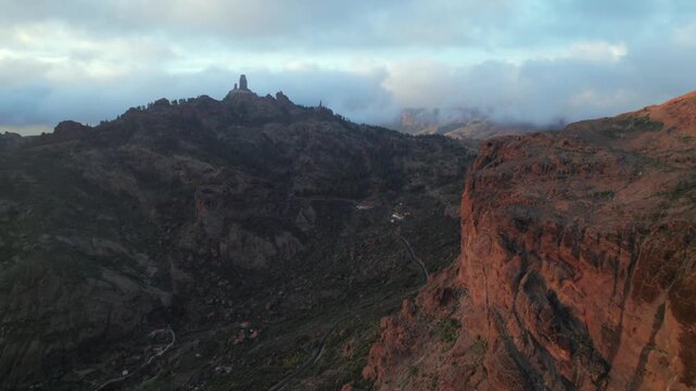 Beautiful aerial view flying over the mountains of Tejeda during a colorful sunset, showing the iconic Roque Nublo in Gran Canaria