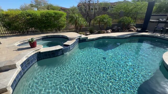 An aerial view of a desert landscaped backyard in Arizona, featuring a travertine pool deck with spa, outdoor BBQ and fireplace.