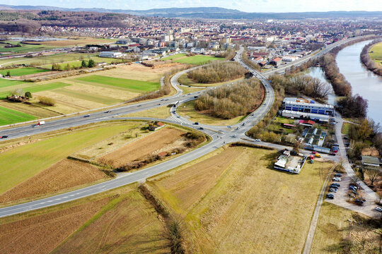 Aerial view of the town of Buttenheim featuring the Regnitz river, highway junctions, and sprawling agricultural fields under a clear sky in Buttenheim, Bavaria, Germany.