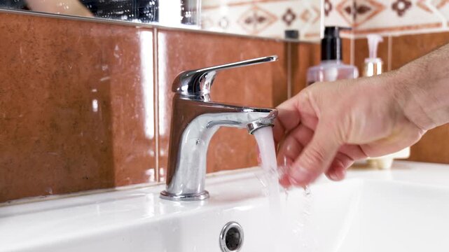 Close-up of a person cleaning a transparent dental aligner under running tap water in a bathroom sink.