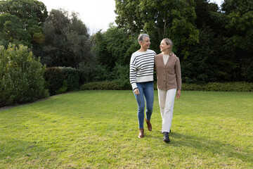 Fototapeta premium Senior and middle-aged women walking on manicured lawn in private garden wearing ankle boots