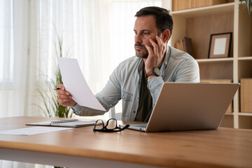 Naklejka premium Thoughtful serious young man lost in thoughts in front of laptop, focused businessman thinking of problem solution, worried puzzled man looking at paper report