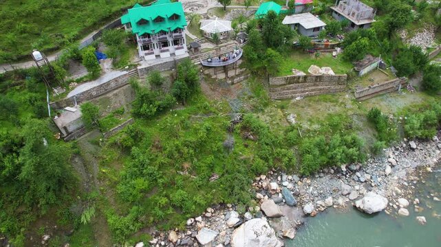 Aerial drone shot pan up reveal from parvati beas river to home house situated on the side of himalaya mountain with more homes houses nearby showing a vacation spot