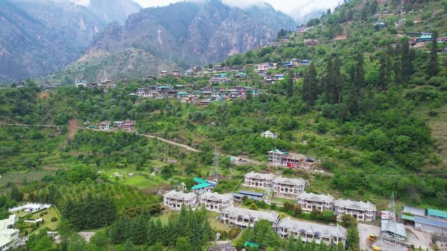 Aerial drone shot quick pan up from Parvati beas river to kasol town located on himalaya mountain slope with lush green mountains in the distance
