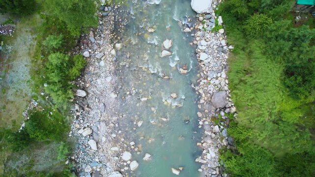 aerial drone shot straight down on rapidly flowing water of parvati beas river filled with stones surrounded by trees showing the cool fresh waters of Indian hill stations