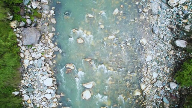 aerial drone shot straight down on rapidly flowing water of parvati beas river filled with stones surrounded by trees showing the cool fresh waters of Indian hill stations